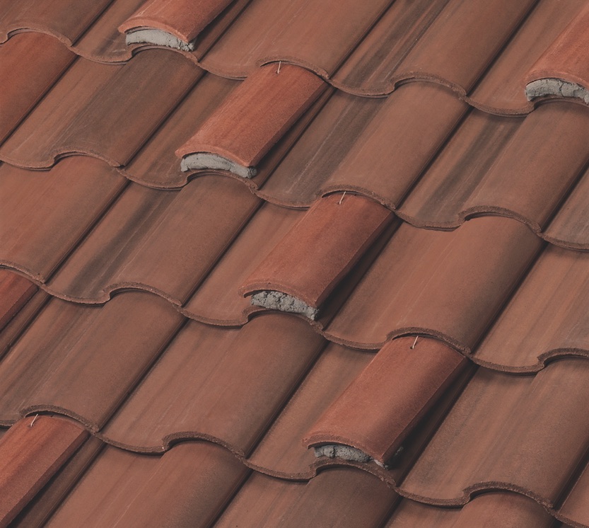 Close-up view of overlapping reddish-brown ceramic roof tiles arranged in a wavy pattern, showing texture and weathered edges.