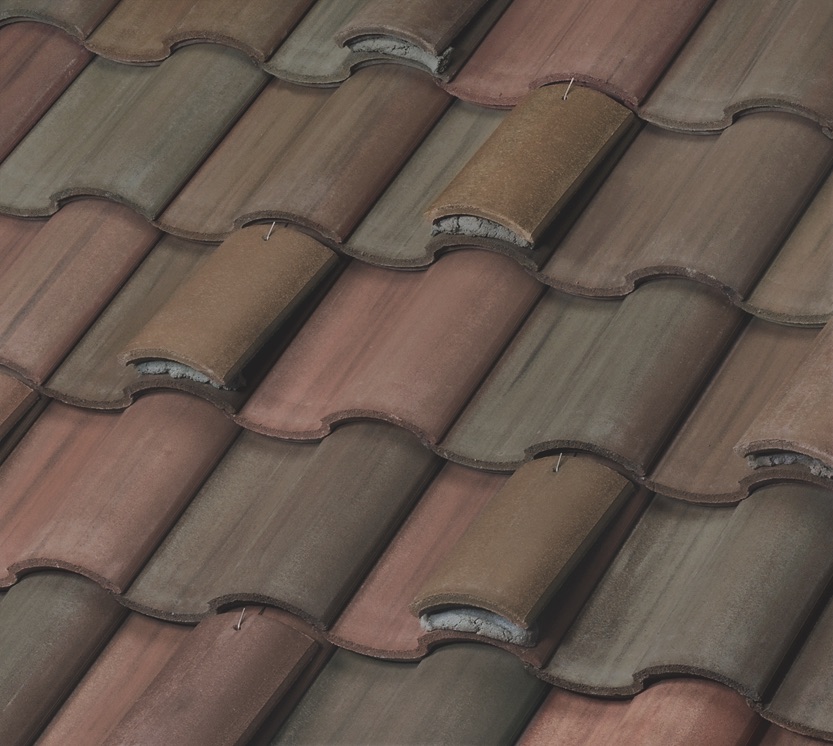 Close-up of a roof with overlapping, curved ceramic tiles in shades of brown and reddish-brown, arranged in a repeating pattern. The surface shows some signs of wear and weathering.
