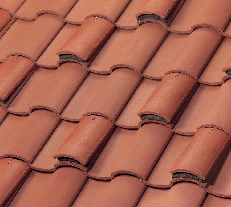 Close-up view of overlapping red clay roof tiles arranged in a wavy pattern, showing the texture and alignment of the tiles.