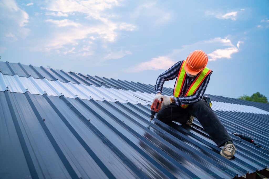 Worker installs metal roofing material using a electric tool
