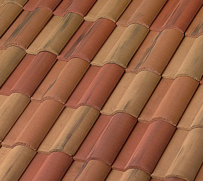 Close-up view of a rooftop covered with overlapping terracotta tiles in shades of reddish brown and tan, arranged in a repeating wave-like pattern.