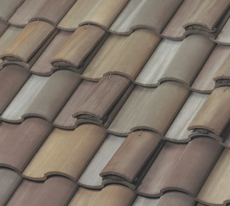 Close-up of overlapping, curved clay roof tiles in shades of brown, tan, and gray, arranged in a staggered pattern on a sloped roof.