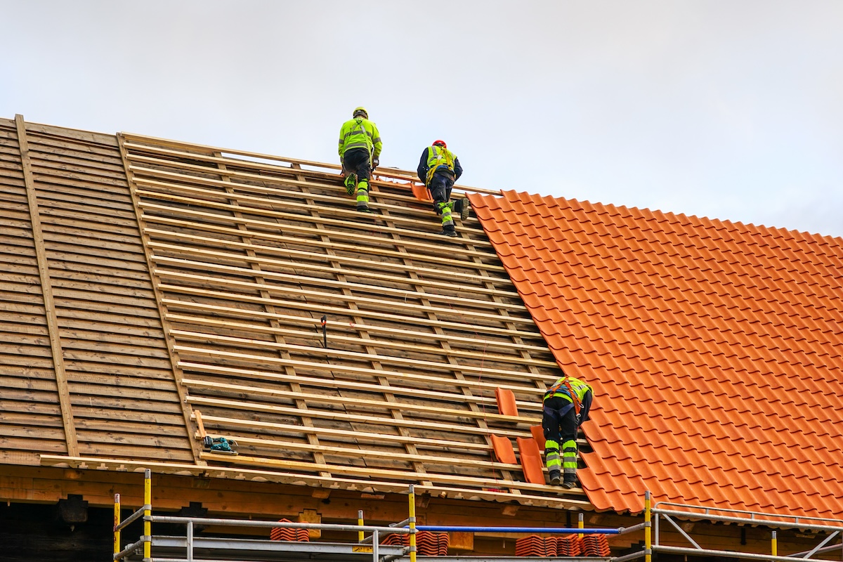 Clay tile roof replacement, three workers laying new clay tile roof, replacement of clay tiles roof