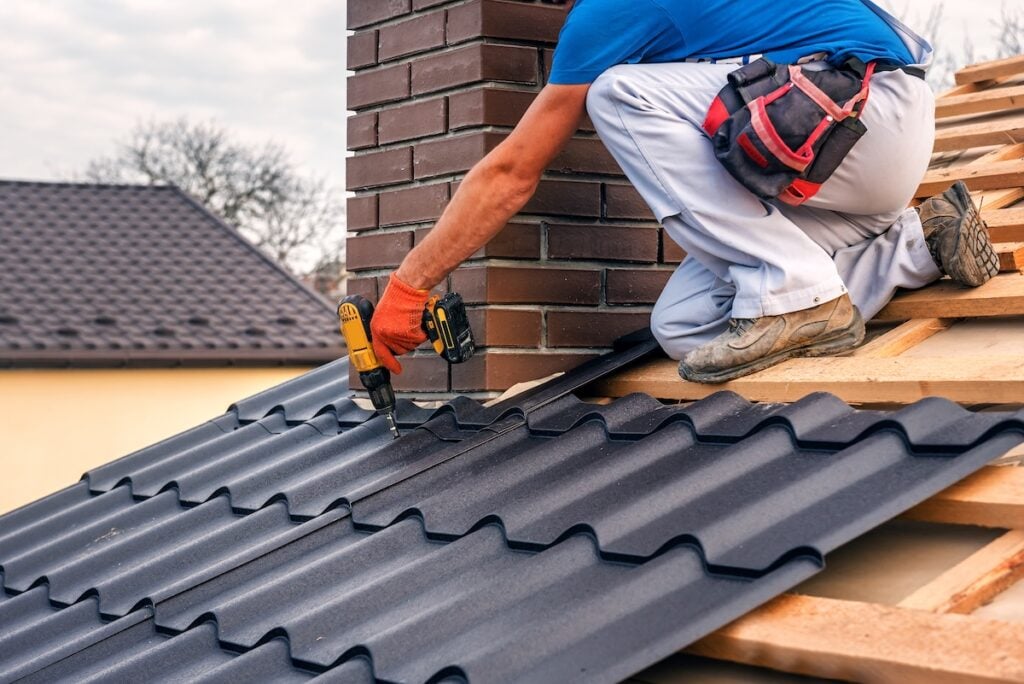 Roofer using a tool to install metal roofing on house