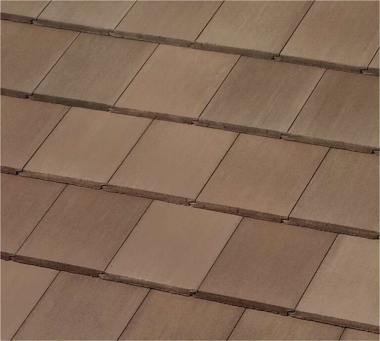 Close-up view of brown rectangular roof tiles arranged in an overlapping pattern, creating a textured, uniform surface. The tiles have slight color variations and visible shadow lines between rows.