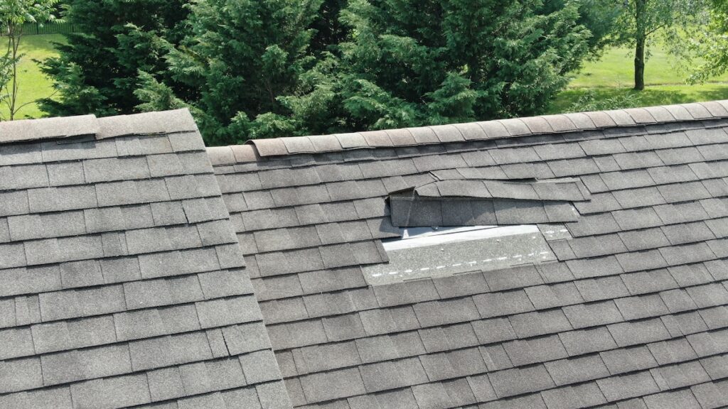 A house roof with several missing and damaged asphalt shingles, exposing a patch of the underlying structure