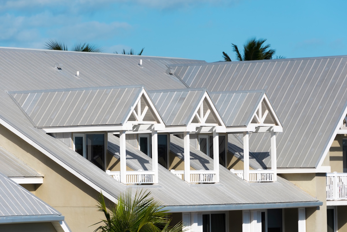 A close-up of a modern house's metal roof with three identical dormer windows, white trim, and a light beige exterior