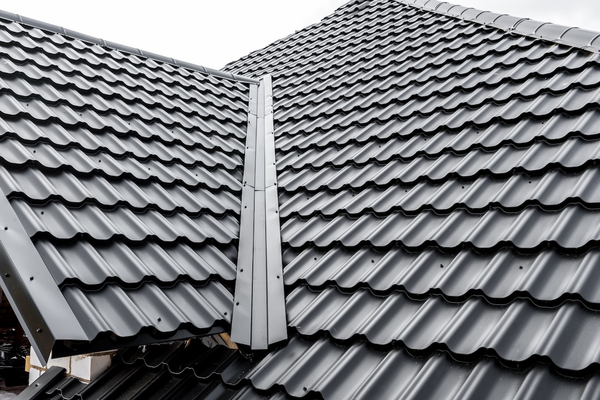 Close-up view of a house roof with shiny, black, wavy metal roofing sheets and a central metal ridge cap