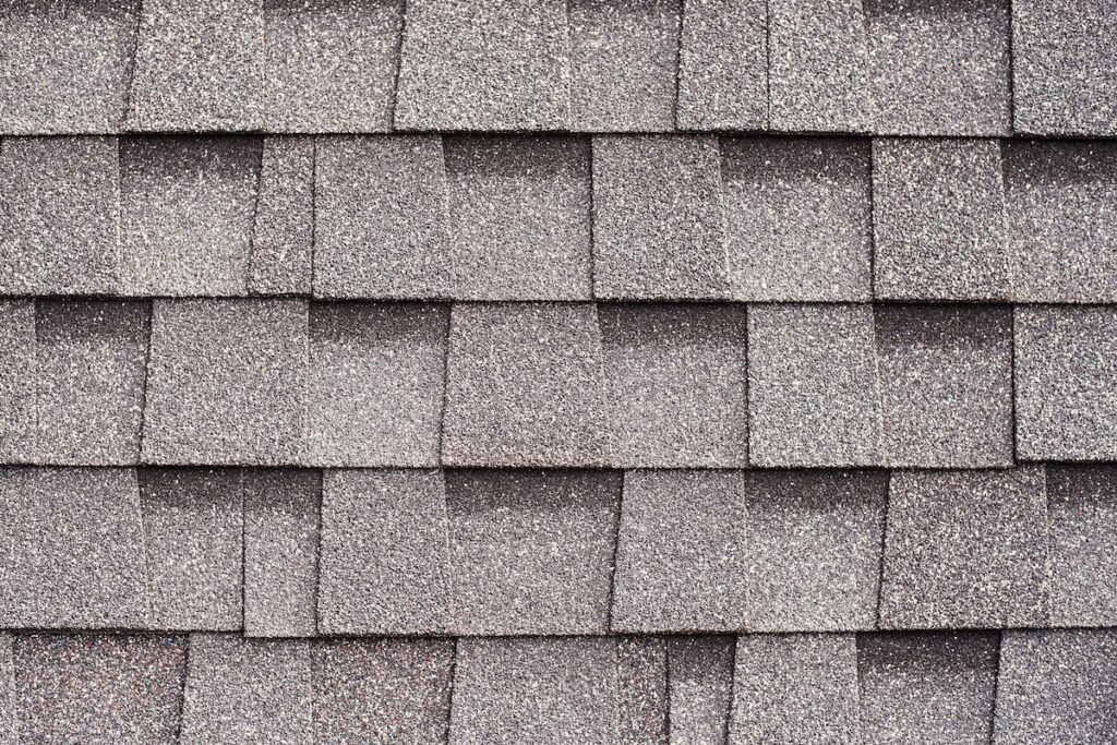 Close-up view of textured, overlapping architectural shingles in a gray color, showing the pattern