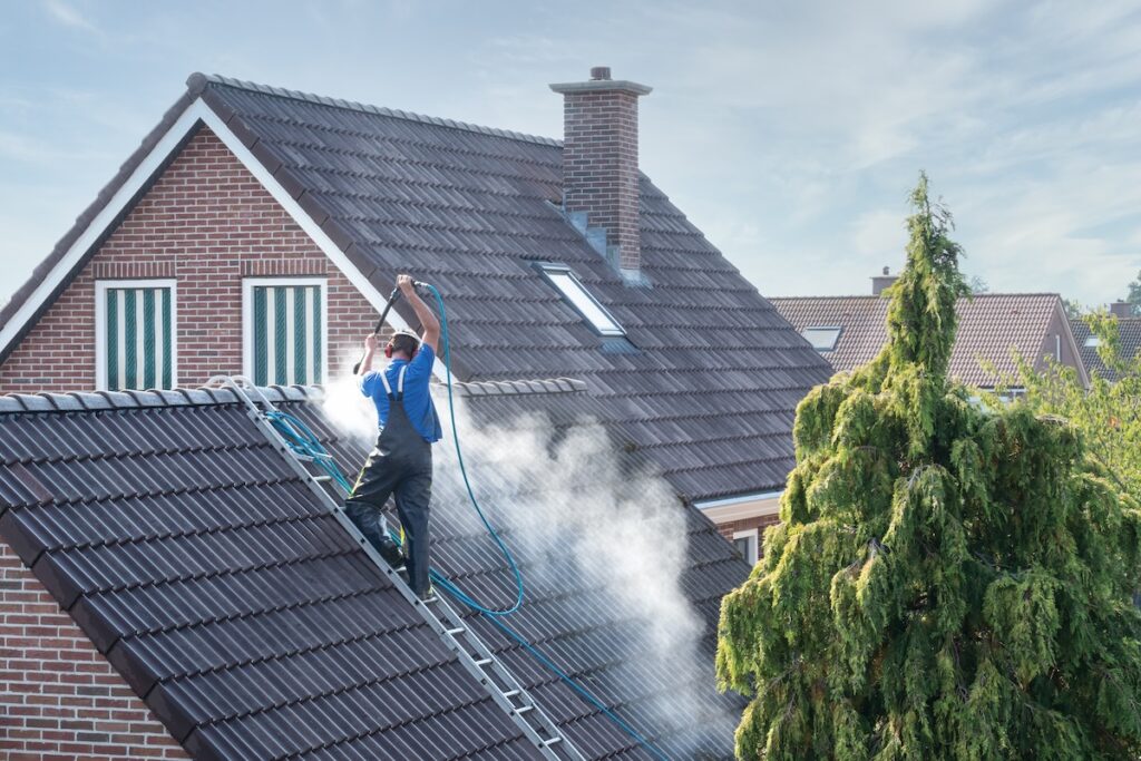 Cleaner with pressure washer at roof of house cleaning the roof tiles