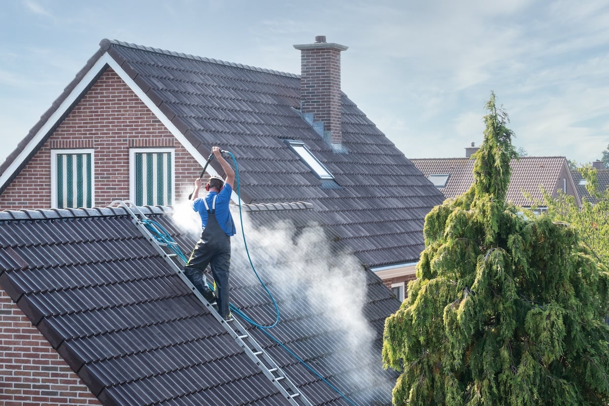 Cleaner with pressure washer at roof of house cleaning the roof tiles