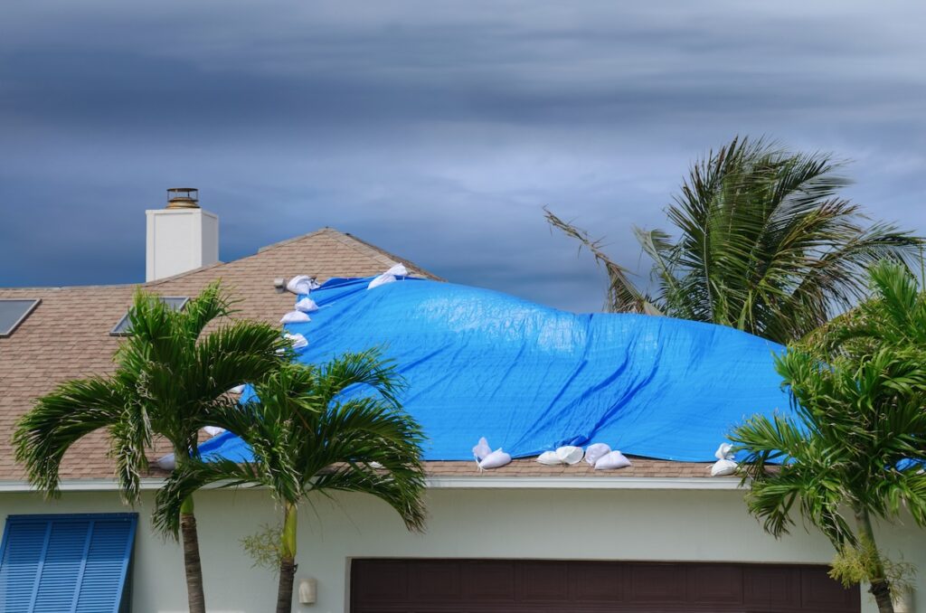 A blue tarp secured with sandbags covers part of a house roo
