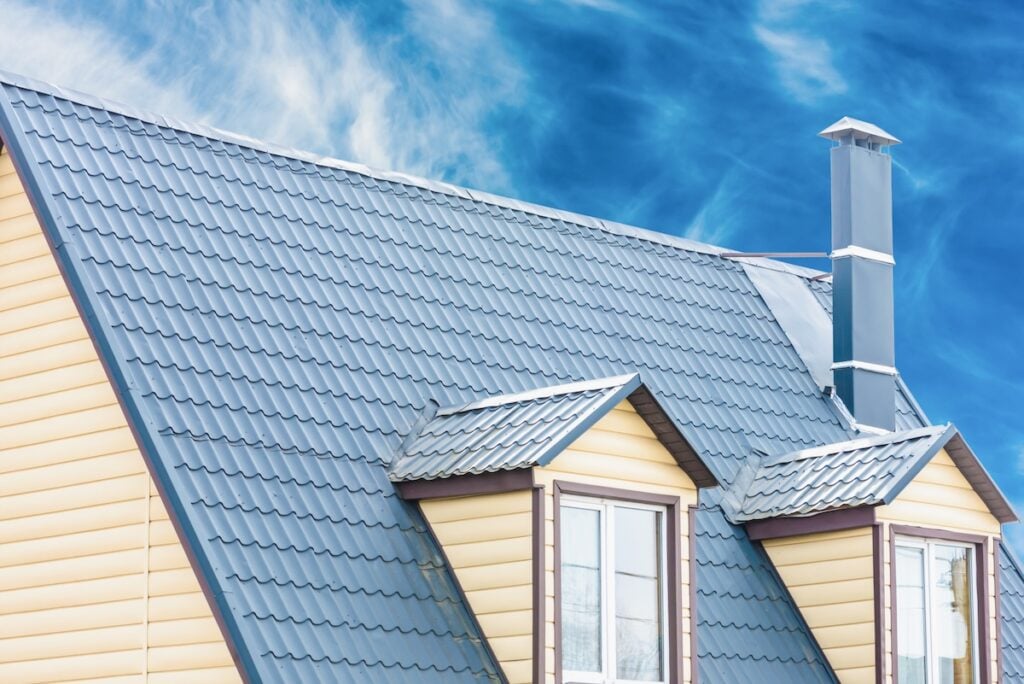A sloped metal roof, reflecting popular types of metal roofs in Florida, with two dormer windows and a chimney on a yellow house