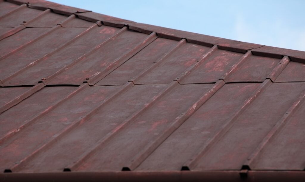 Close-up view of a red metal roof with visible seams and panels with a weathered surface