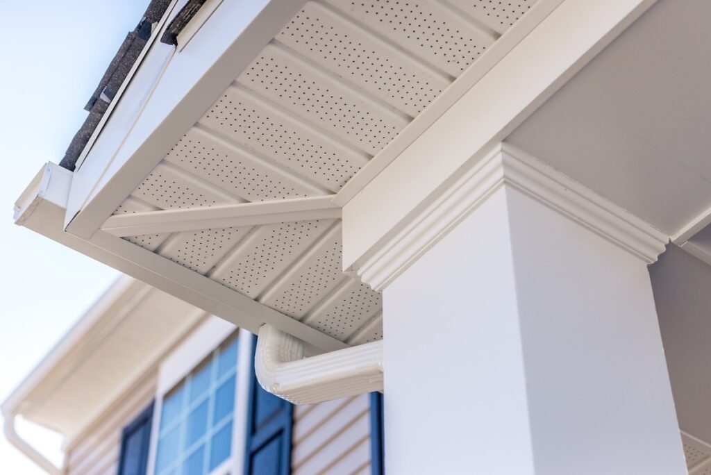 Close-up view of a house’s white soffit, fascia, column, and gutter system highlights exterior architectural details