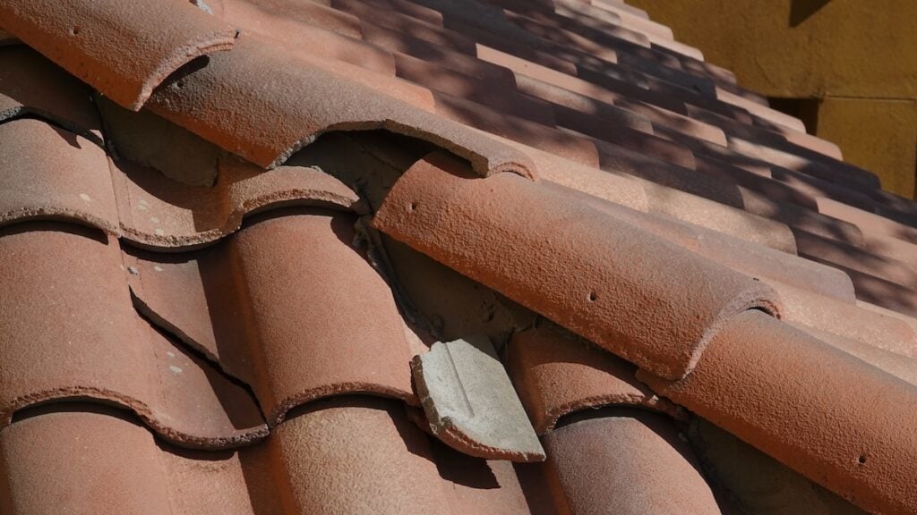 Close-up of a terracotta tiled roof with curved overlapping tiles; one grayish tile in the center hints at recent storm damage roof repair.