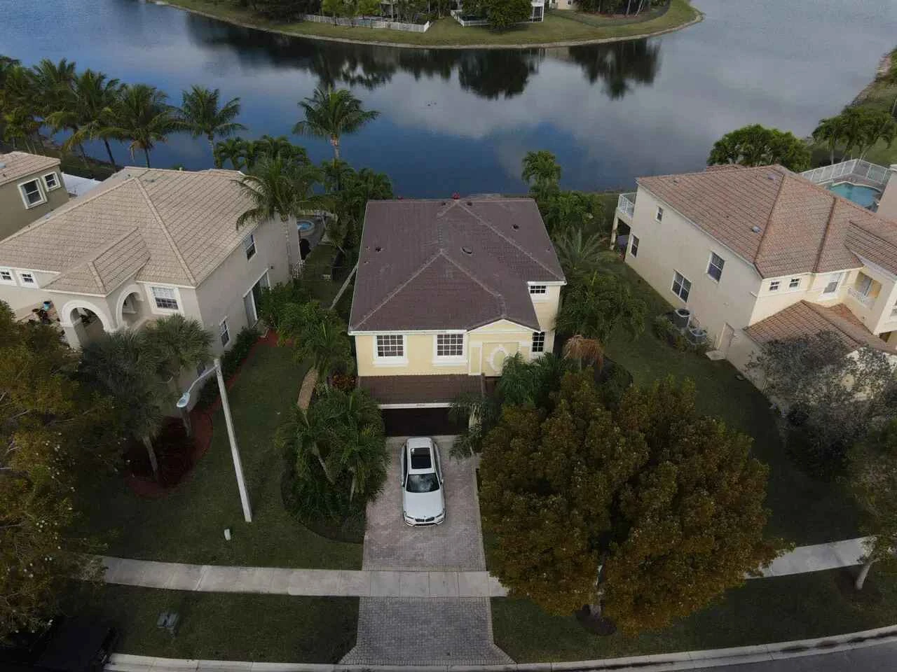 Aerial view of a suburban house with a car parked in the driveway, surrounded by trees and neighboring homes, situated near a lake.