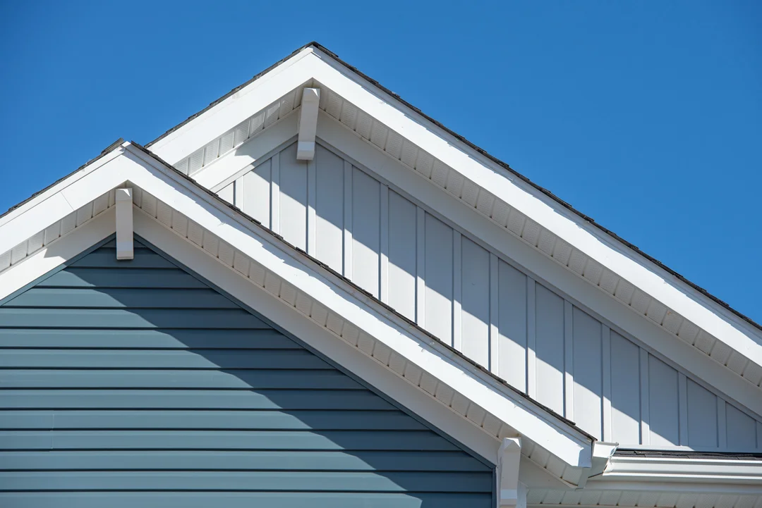 Two gabled rooftops with white trim and contrasting siding, one in light blue and the other in white, are shown against a clear blue sky.