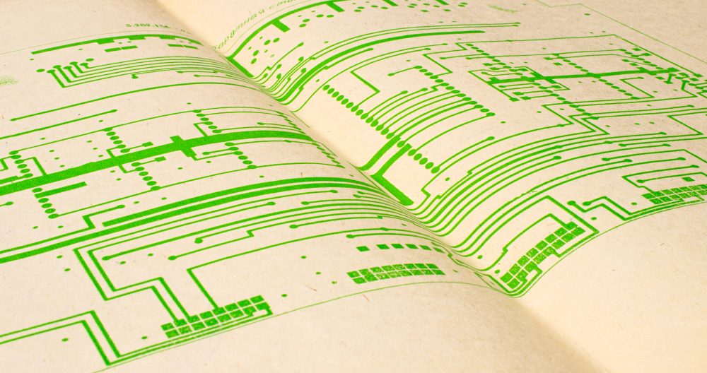 Close-up of a book open to pages showing green printed circuit board schematics or electronic diagrams on a cream-colored background.
