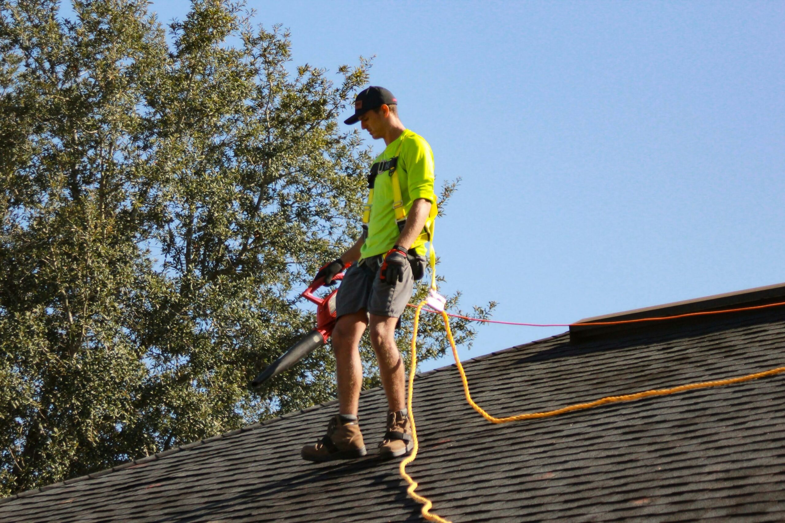 Professional roofer cleaning a residential metal roof with proper safety equipment and cleaning tools