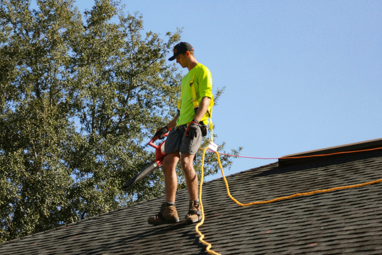 Professional roof technician wearing safety gear while cleaning a metal roof