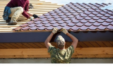 Team of roofers collaborating on metal roof installation project showing proper underlayment and panel placement
