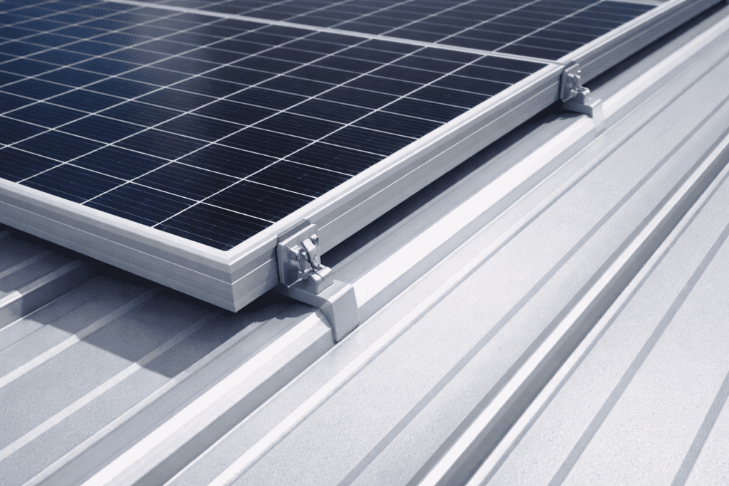 Close-up of solar panels mounted on a metallic, ribbed rooftop, showing the panels' metal frames and mounting brackets under bright daylight.