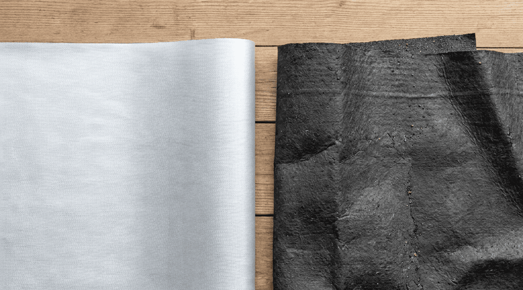 Two sheets of material on a wooden surface: one is smooth, light gray, and metallic-looking, while the other is dark, rough, and textured.