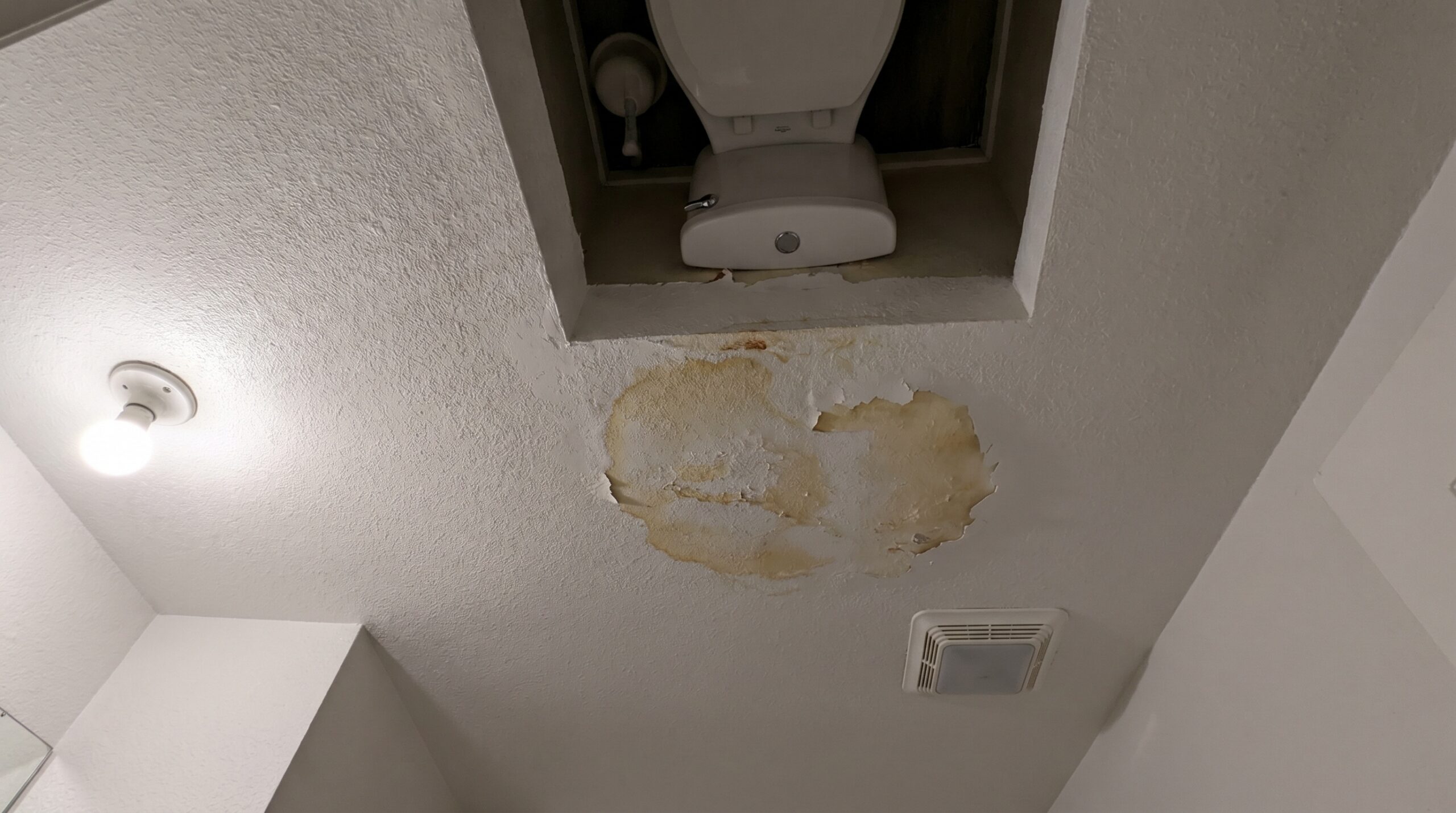 Bathroom ceiling with water stain below toilet